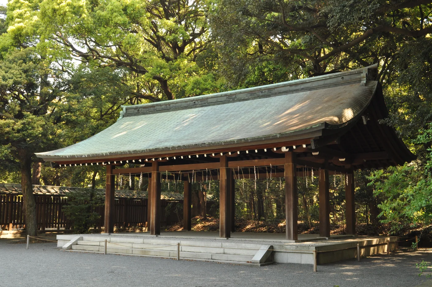 A wooden shrine structure with a curved green roof among trees in the grounds of Meiji Jingu in Tokyo.